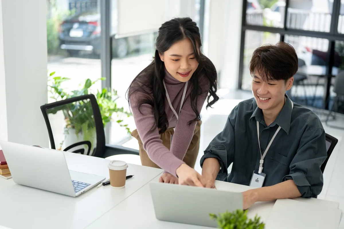 Two marketing team members reviewing work on a laptop together in a bright office